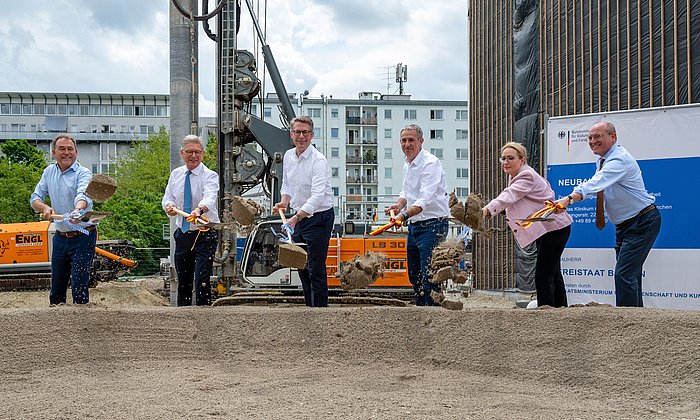 Die Rednerinnen und Redner setzen den ersten Spatenstich für das Gebäude.
