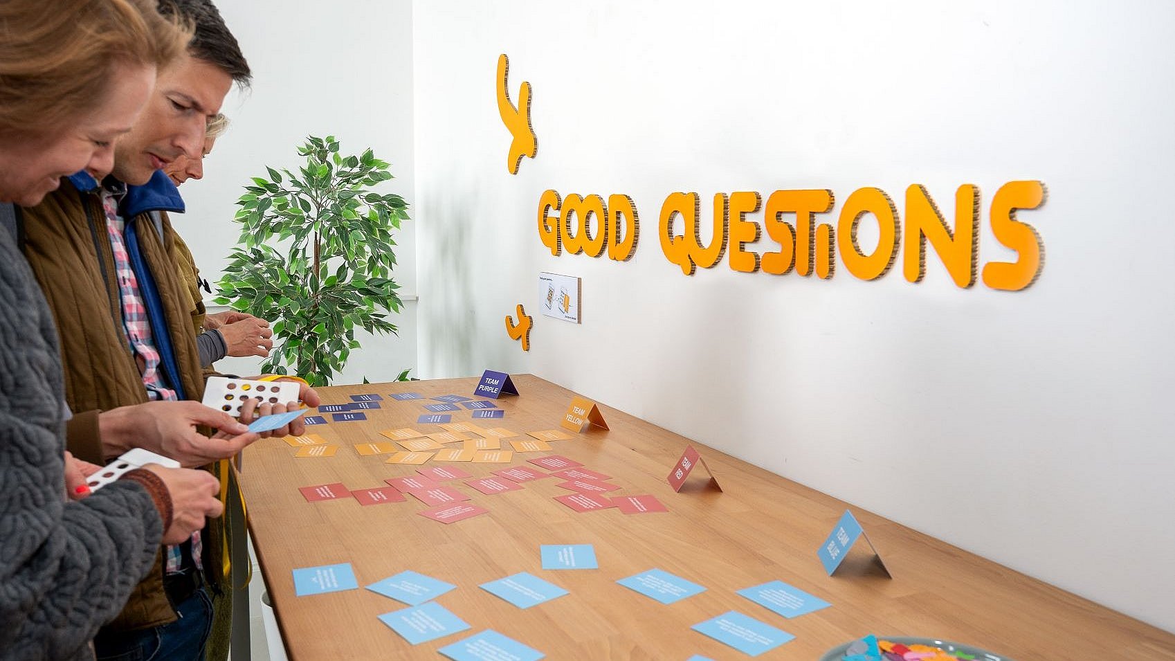 Besucherinnen und Besucher der Veranstaltung "Creative Collisions" stehen an einem Tisch, auf dem kleine Kärtchen mit Fragen ausgelegt sind.