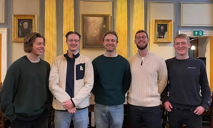 Group photo of the five founders of wahl.chat Sebastian Maier, Anton Wyrowski, Michel Schimpf, Robin Frasch and Roman Mayr, standing in a prestigious room in front of golden columns and paintings on the walls