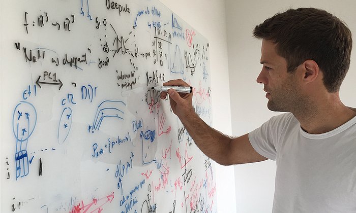 Das Bild zeigt Prof. Fabian Theis, beim Schreiben von Formeln an eine Tafel.