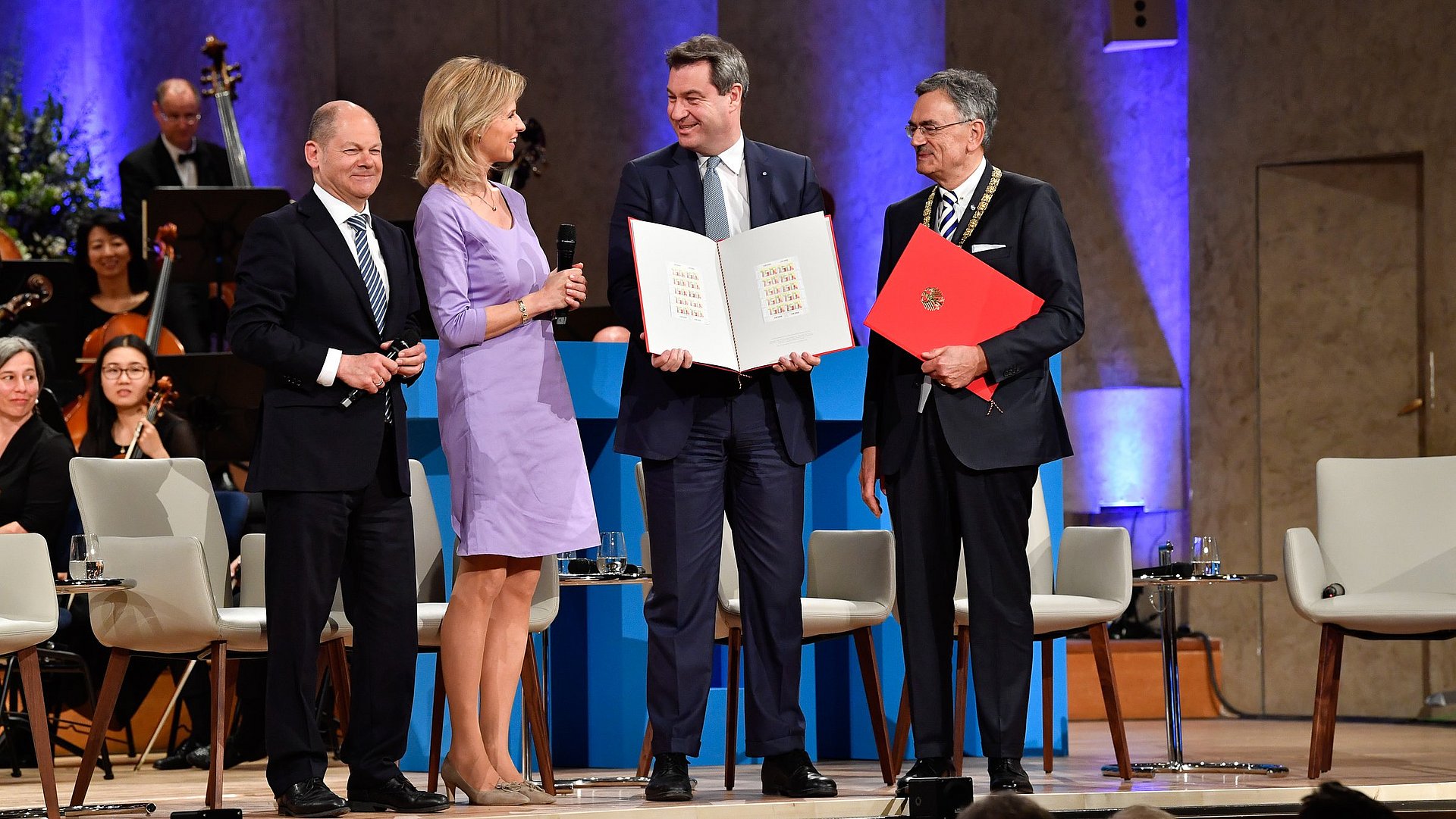 Olaf Scholz, Anouschka Horn, Markus Söder und Wolfgang A. Herrmann (v.l.n.r.) stehen zusammen auf einer Bühne; Söder und Herrmann halten aufgeschlagene Mappen in ihren Händen. Grund ist der Festakt im Jahr 2018 anlässlich des 150jährigen Jubiläums der Technischen Universität München im Herkulessaal der Münchner Residenz.