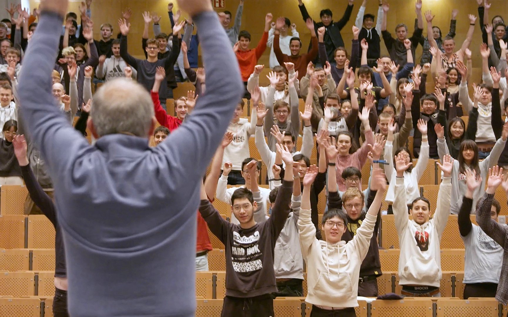 Aktive Pause während der Vorlesung: Prof. Diepold ist im Hörsaal von hinten zu sehen, wie er die Arme nach oben reckt, vor ihm Studierende, ebenfalls mit nach oben gereckten Armen