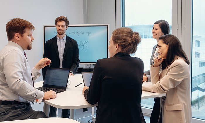 Mehrere Personen stehen in einem Seminarraum am Tisch und nehmen an einem Workshop teil.
