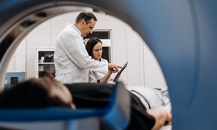 Blick auf einen Patienten und eine Ärztin und einen Arzt durch ein MRT-Gerät