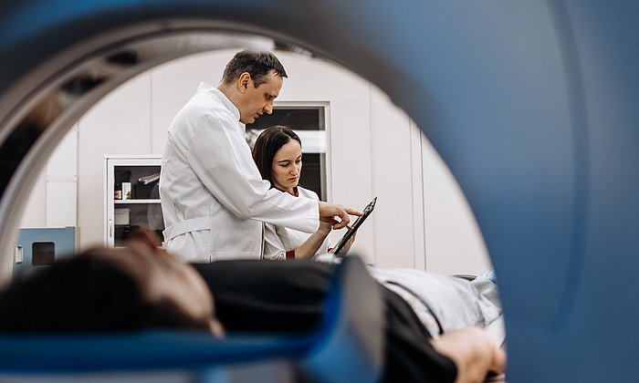 View of a patient and two doctors through an MRI machine.