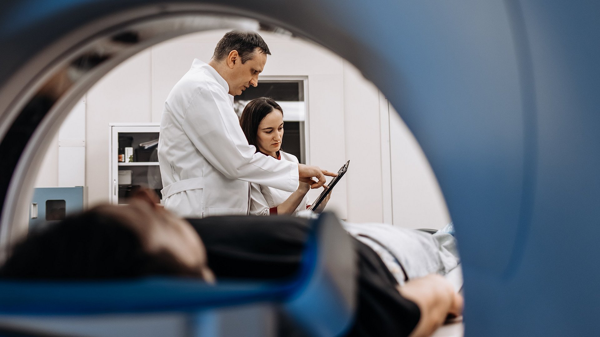 Blick auf einen Patienten und eine Ärztin und einen Arzt durch ein MRT-Gerät