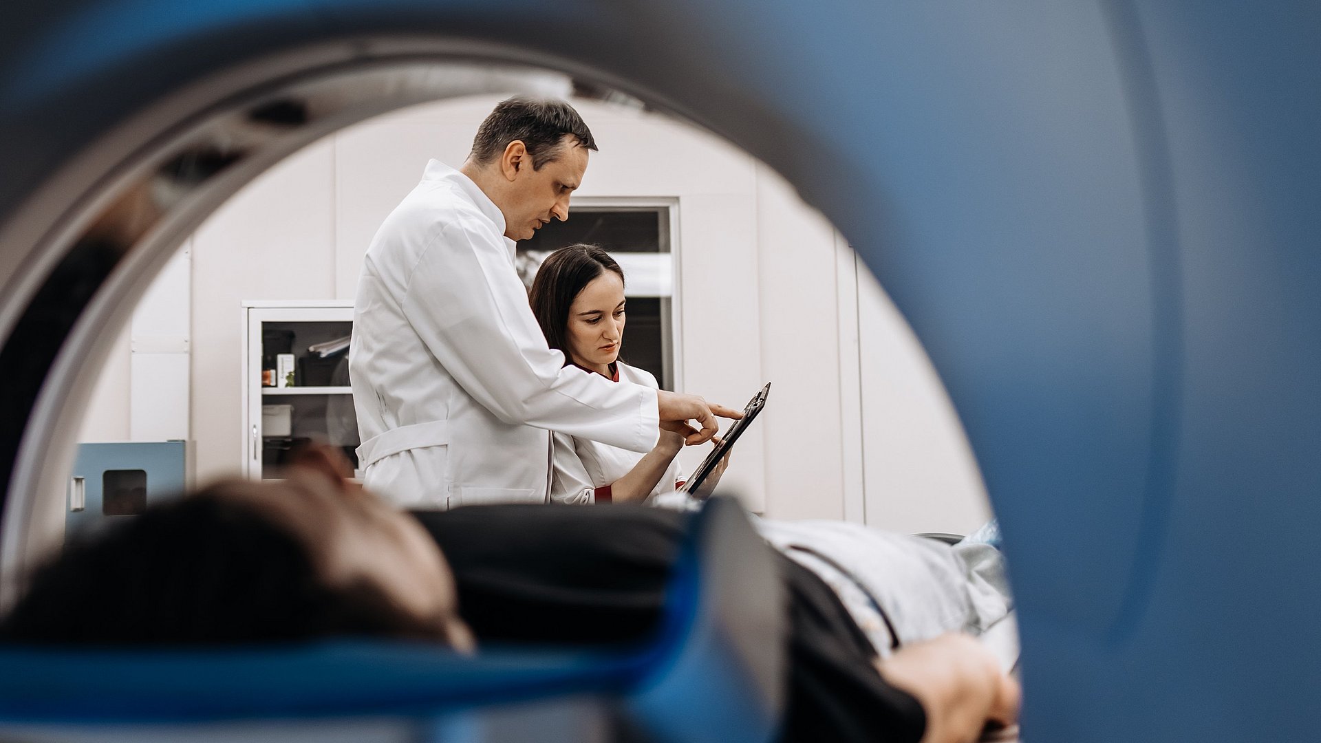 View of a patient and two doctors through an MRI machine.
