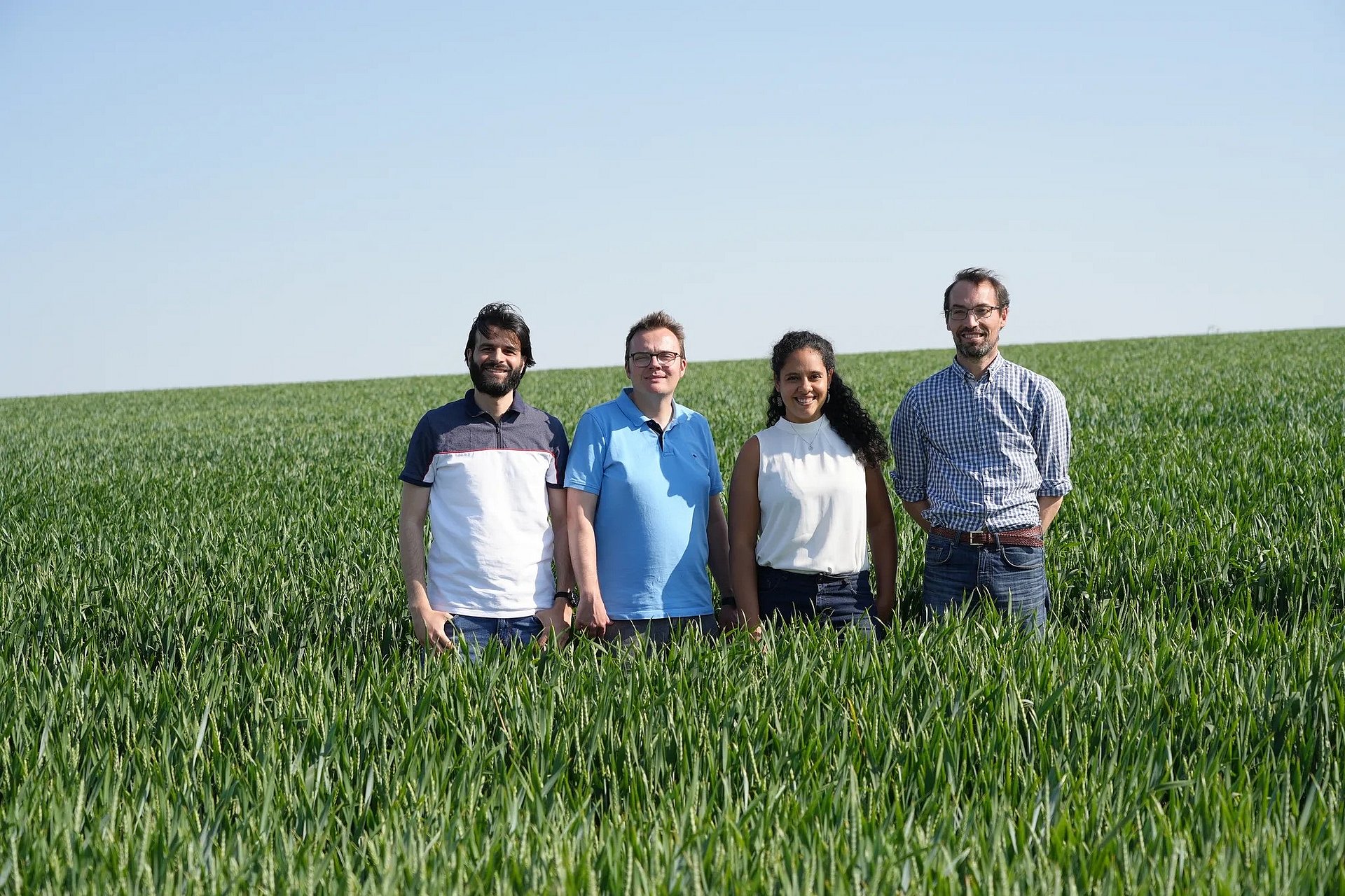 Vier Personen stehen im Feld und blicken in die Kamera.