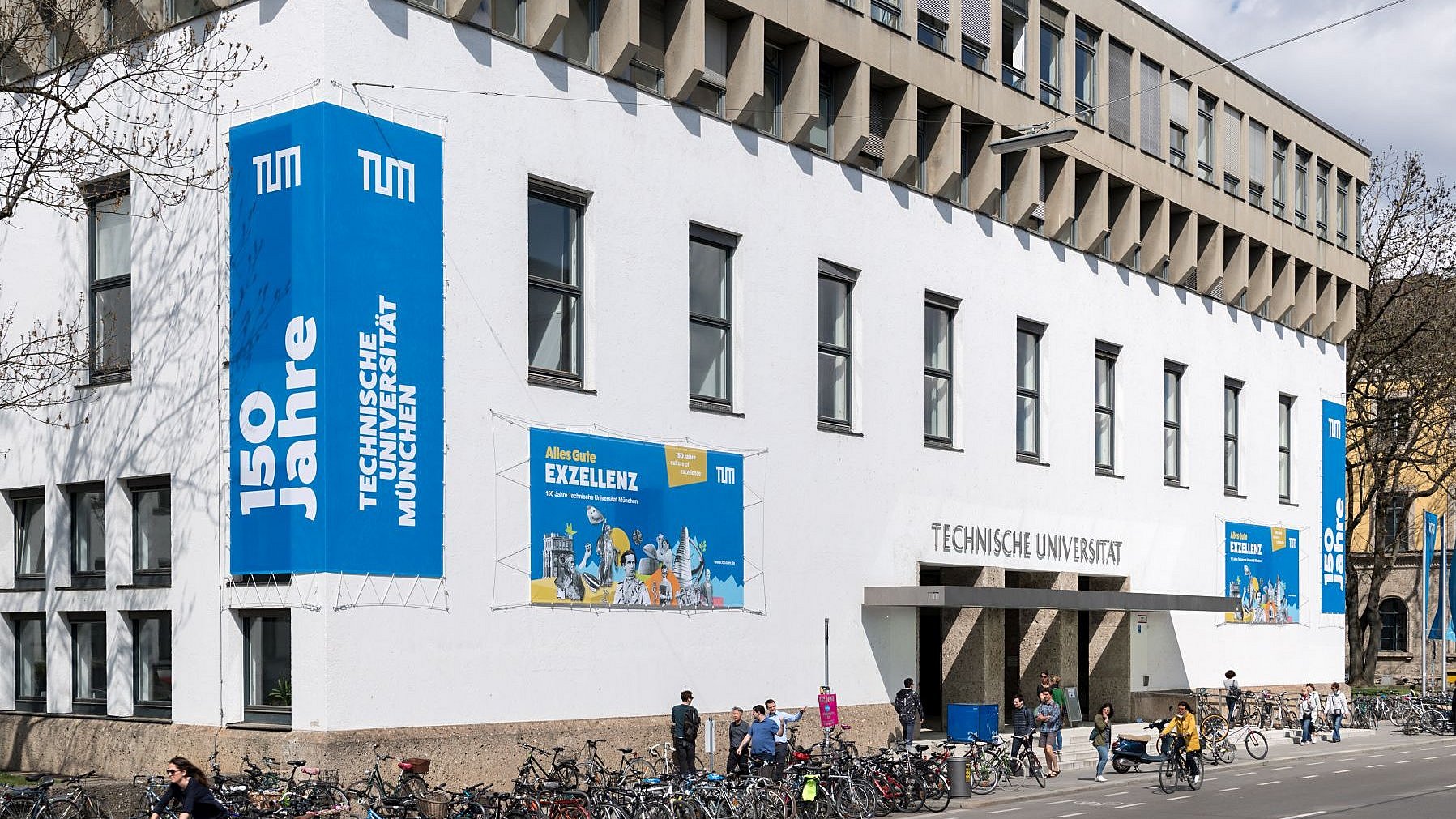 Außenfassade des Stammgeländes der TUM in der Innenstadt München. An den Wänden hängen blaue Banner mit weißer Beschriftung zum 150-jährigen Jubiläum der Universität im Jahr 2018.
