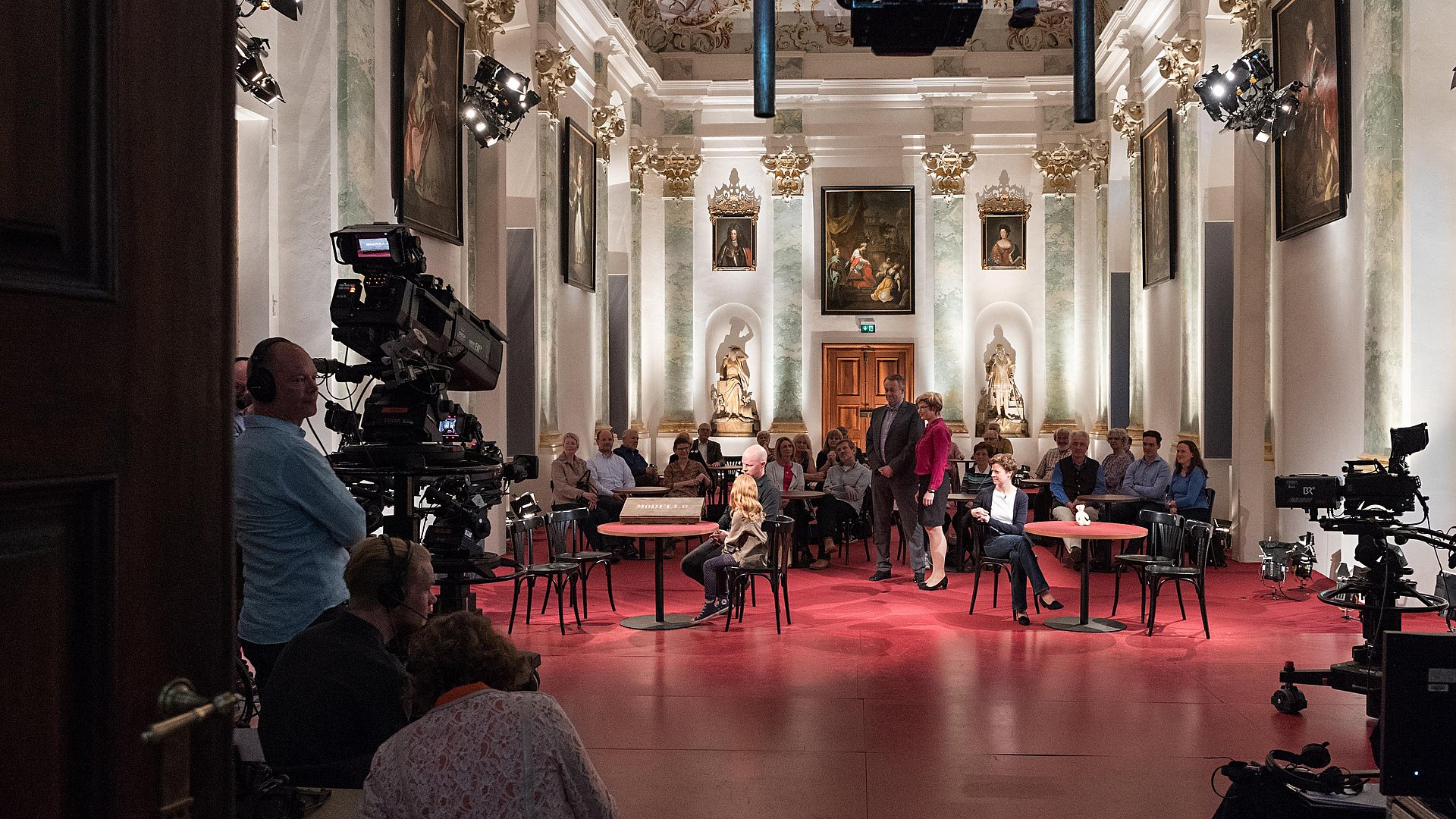 Personen mit Kameras filmen eine Sendung in einem Saal der Akademie.