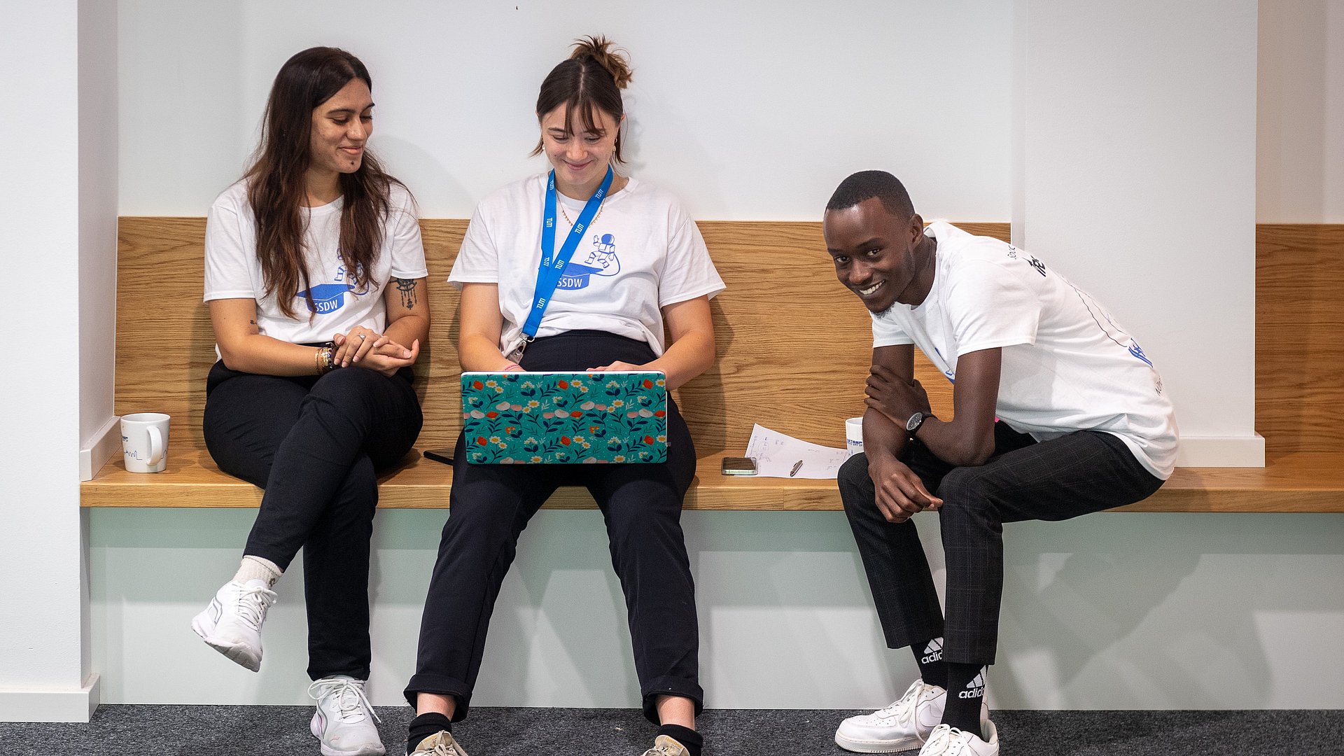 Three participants are sitting smiling in a quiet corner, working on their laptops