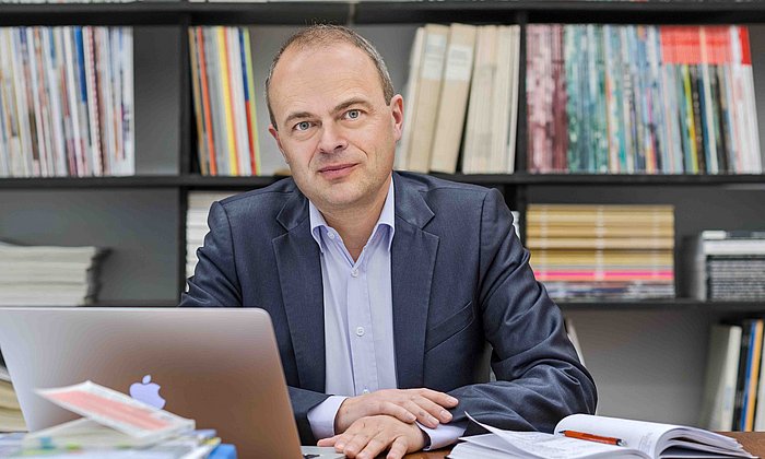 Prof. Stephan Trüby vor einem Bücherregal in seinem Büro.