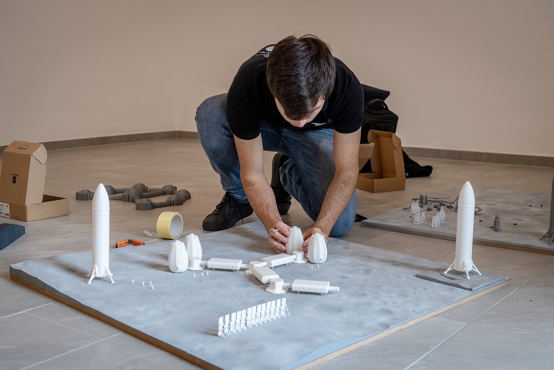 Student klebt Teile einer Mondsiedlung aus dem 3D-Drucker auf eine Mondlandschaft