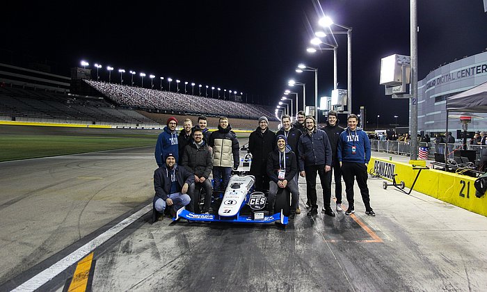 A group of scientists stand around a formula racing car.