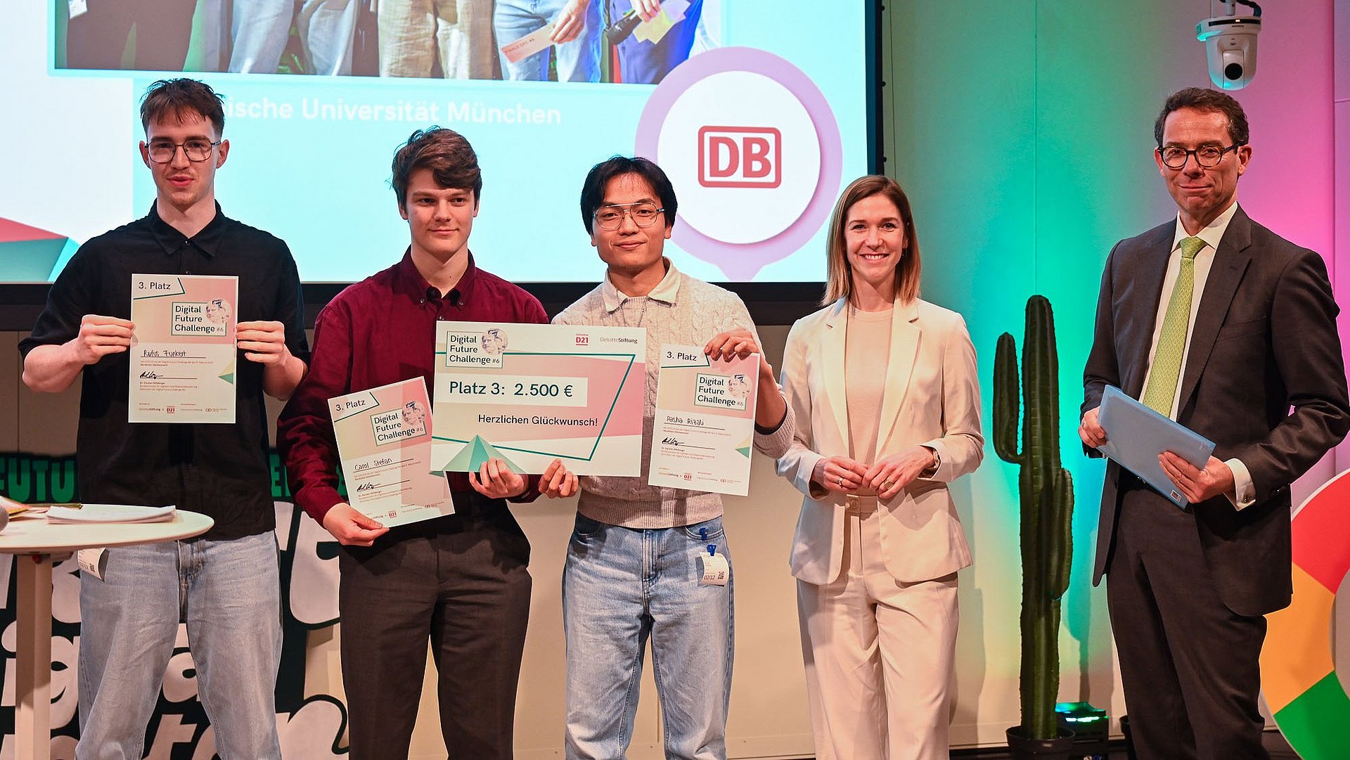 The three students of the “RollsRoICE” team together with two additional individuals on stage at the final of the Digital Future Challenge 2026, presenting their certificates to the audience.