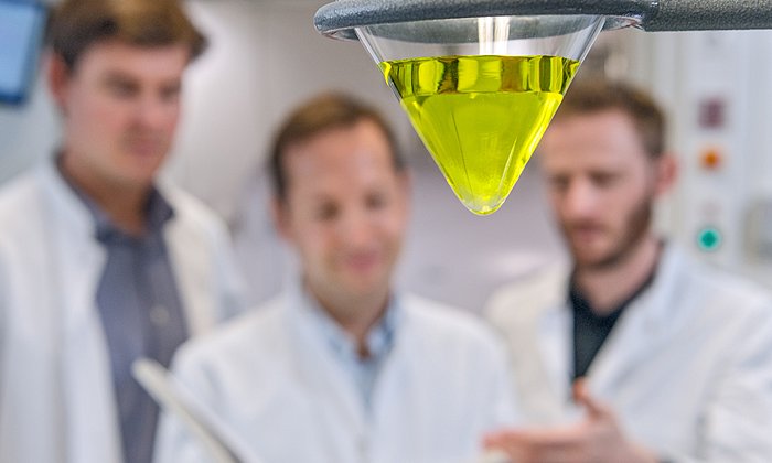 Ein Gefäß mit Zymonsäure. Dahinter sind unscharf die Autoren der Studie zu erkennen.