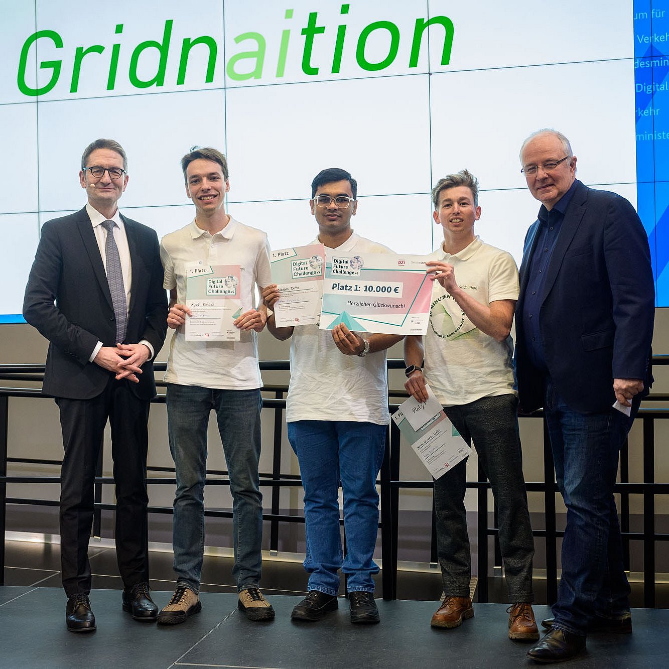 Three students of the “Gridnaition” team on stage at the Federal Ministry for Digital and Transport, holding the winning certificates, with the two laudators to their left and right.