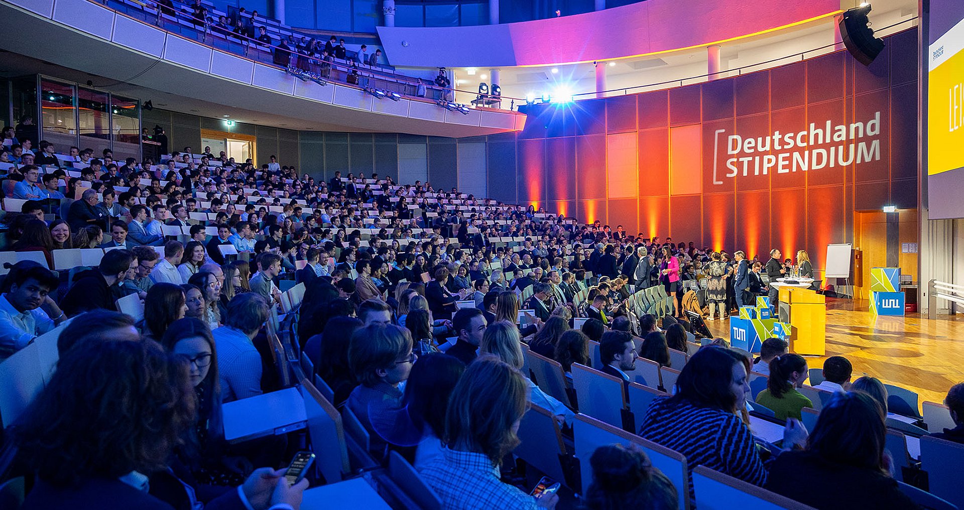  Festively lit lecture hall with a dark, packed auditorium at the ceremony for the Deutschlandstipendium in 2024.