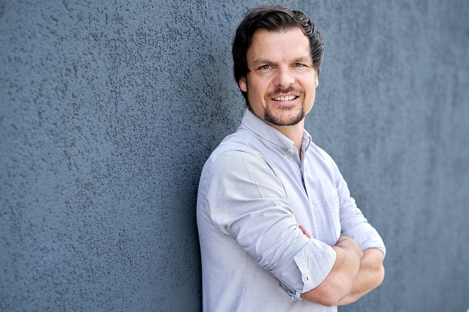 Mann mit hochgekrempeltem Hemd und verschränkten Armen schaut in die Kamera