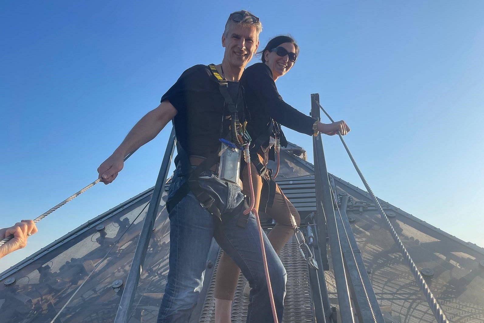 Ein Fördererpaar steht angeseilt auf dem Olympia-Zeltdach und schaut freundlch in die Kamera
