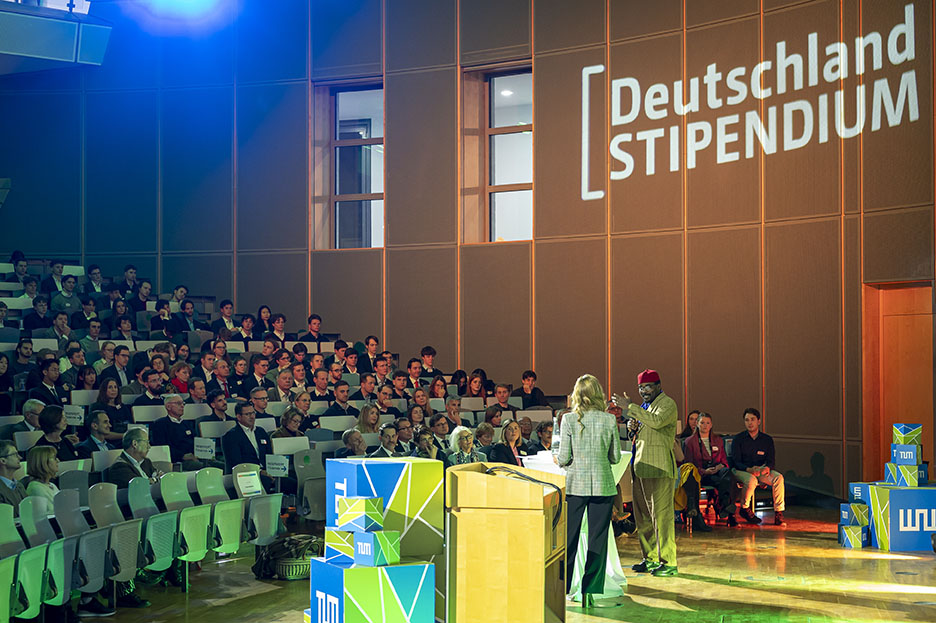 Lecture hall with festive lighting during the ceremony for the Deutschlandstipendium. Well-filled auditorium with presenter and program ambassador Chidera Abonyi President Hofmann in conversation