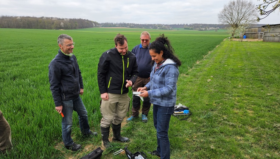 Eine Frau und drei Männer stehen auf einem Acker. Die Frau zeigt den Männern ein Gerät in ihrer Hand. Es handelt sich um das Gerät, dass das NutriSen-Team zur smarten Düngung entwickelt hat.